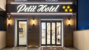 L’extérieur du Petit Hôtel présente un design moderne, avec un panneau néon, des décorations en forme d’étoiles et une entrée bien visible.