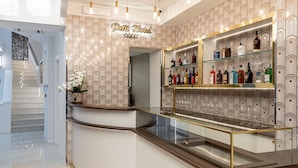 Un hall d’hôtel doté d’un comptoir d’accueil incurvé, d’un escalier et d’un bar, avec un papier peint à motifs et des étagères en verre où sont exposées différentes bouteilles.