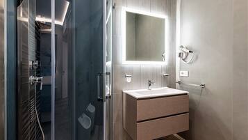 A modern bathroom with a glass shower enclosure, a large mirror, and a built-in sink with a textured cabinet.