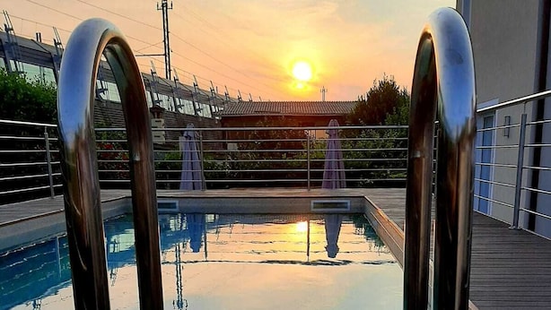 Une piscine entourée de barrières métalliques, bordée d’une terrasse et avec un bâtiment visible à l’arrière-plan.