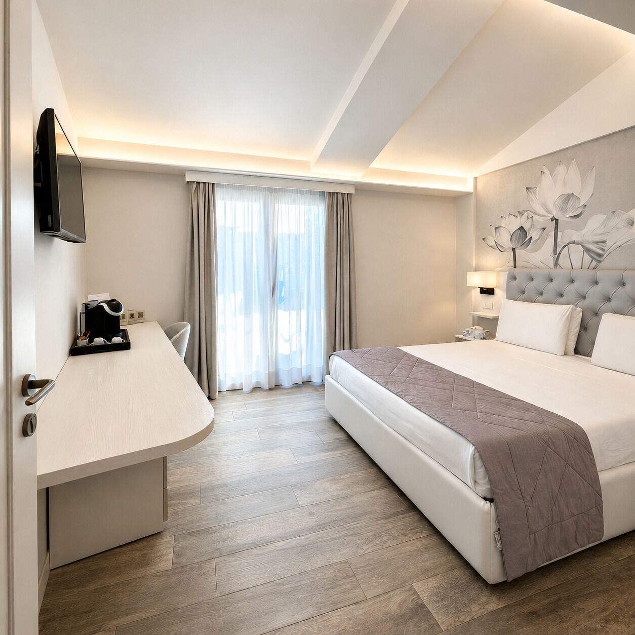 Habitación de hotel con cama, escritorio, silla, televisor y ventana con cortinas.