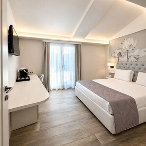 Habitación de hotel con cama, escritorio, silla, televisor y ventana con cortinas.