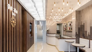 Un hall d’hôtel moderne avec un comptoir d’accueil en bois, un bar et des espaces pour s’asseoir.