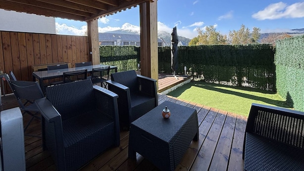 An outdoor patio with wooden flooring, wicker furniture, and a view of a neatly trimmed hedge and distant mountains. - Peaceful Mountain Escape: 2BR Apartment, Terrace, Close to Ski, Free Parking, WiFi (Villard-de-Lans)