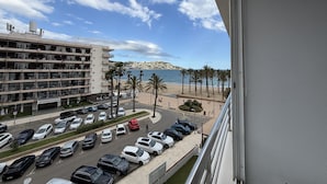 A view of a parking lot with several cars, a building with multiple floors, and a beach with palm trees in the background. - Charming 1-bedroom apartment with pool & garden in Roses Santa-Margarita (Roses)