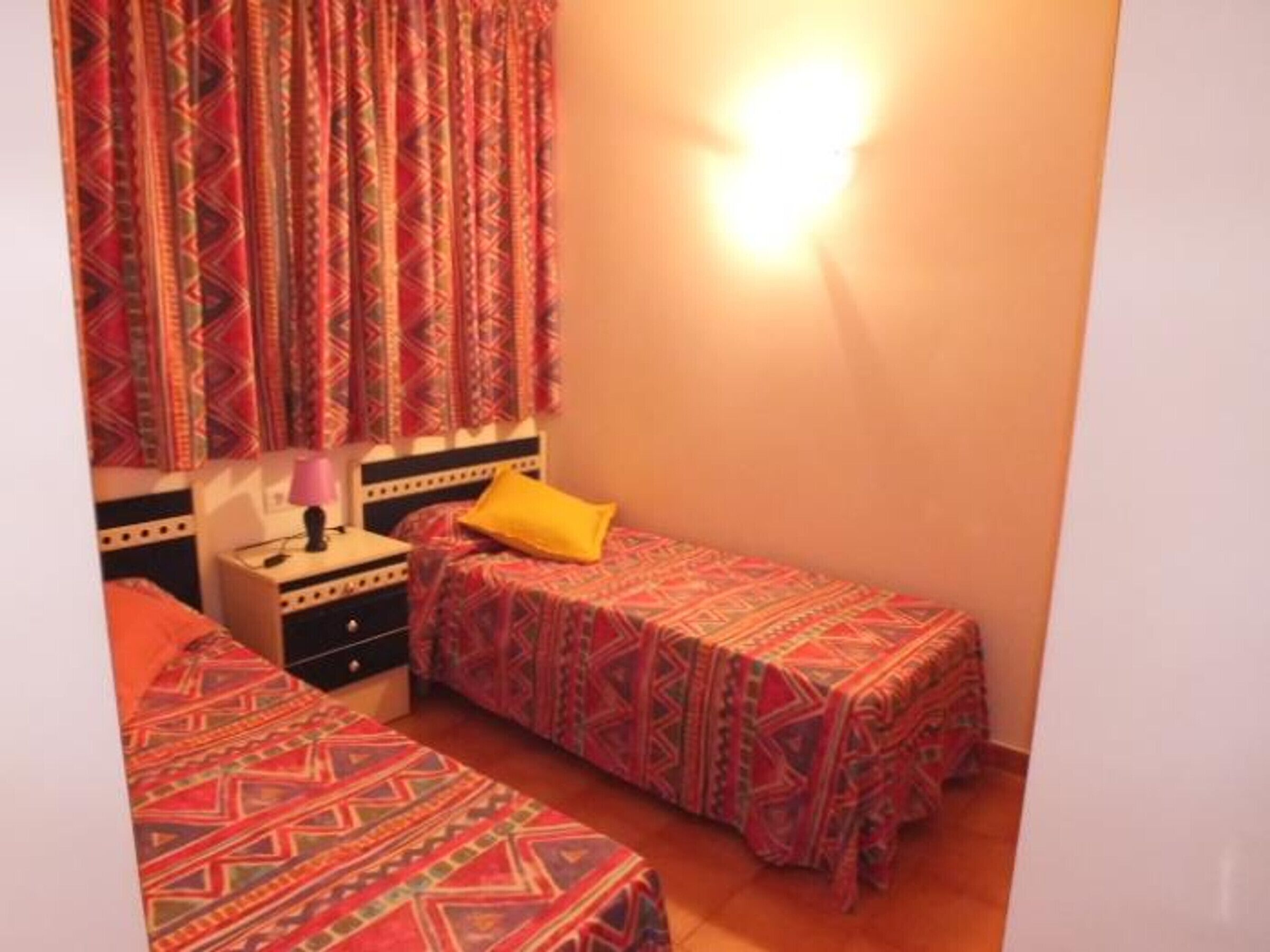 Ein kleines, gemütliches Schlafzimmer mit zwei Einzelbetten, einem Nachttisch und einer Lampe.
