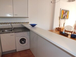 Une cuisine compacte équipée d’un lave-linge, d’un évier et d’un petit coin repas avec une chaise et une table.