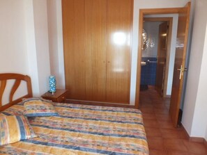 Une chambre à coucher avec un lit, une armoire en bois et une salle de bain visible à travers une porte ouverte.