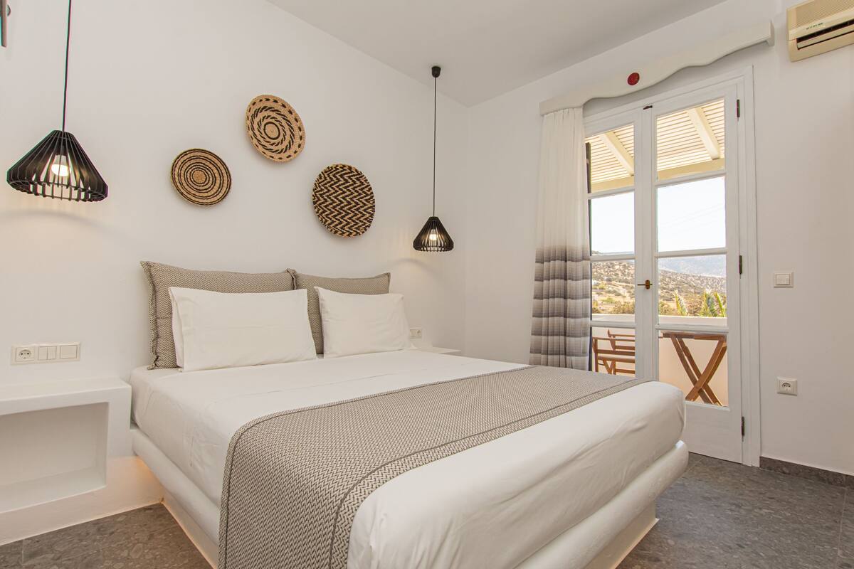 Un dormitorio con cama, mesitas de noche, decoración en la pared y vistas por una puerta.