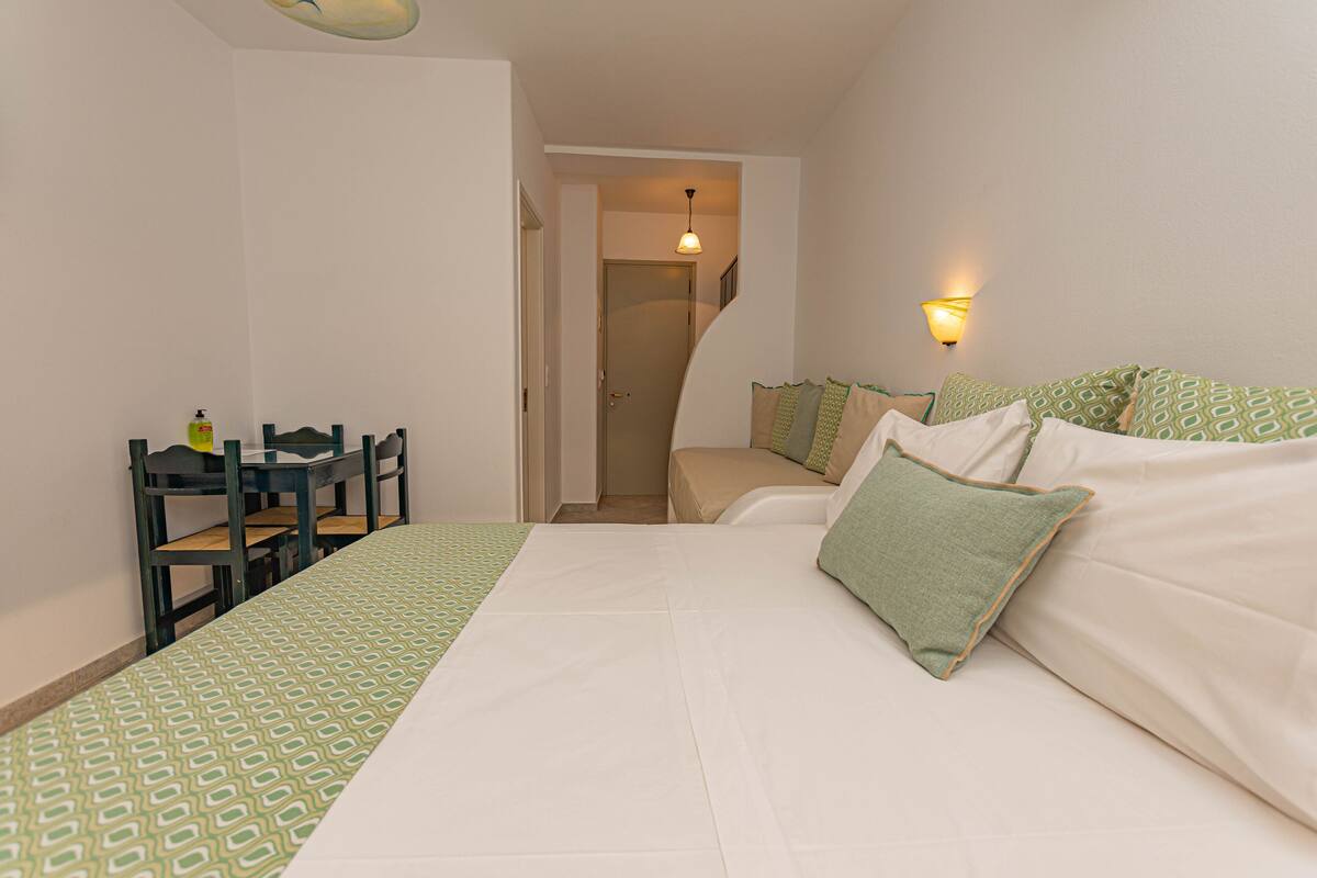 Un dormitorio con cama, escritorio y silla. Hay una puerta que da a otra habitación.