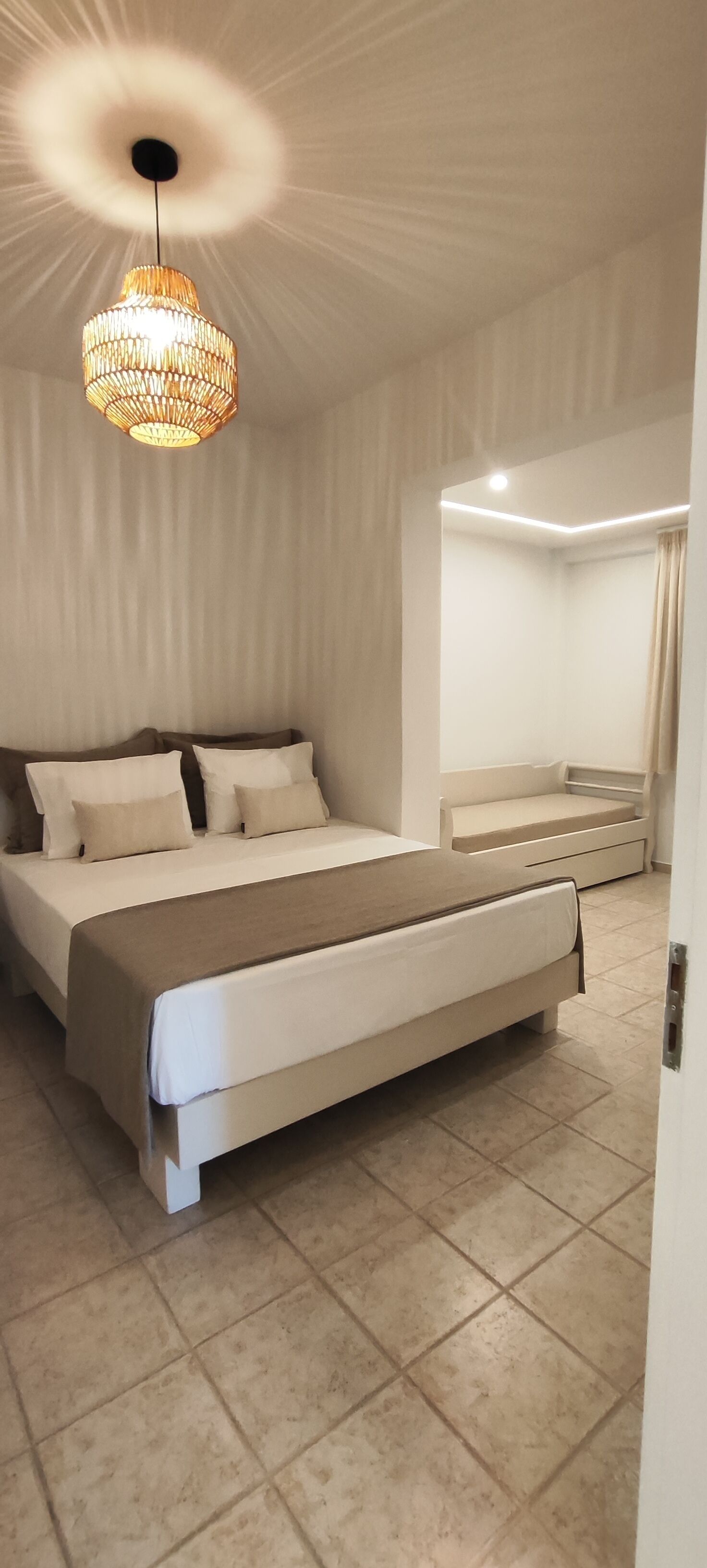 A bedroom with a large bed, a bedside table, a hanging light fixture, and a built-in bench.