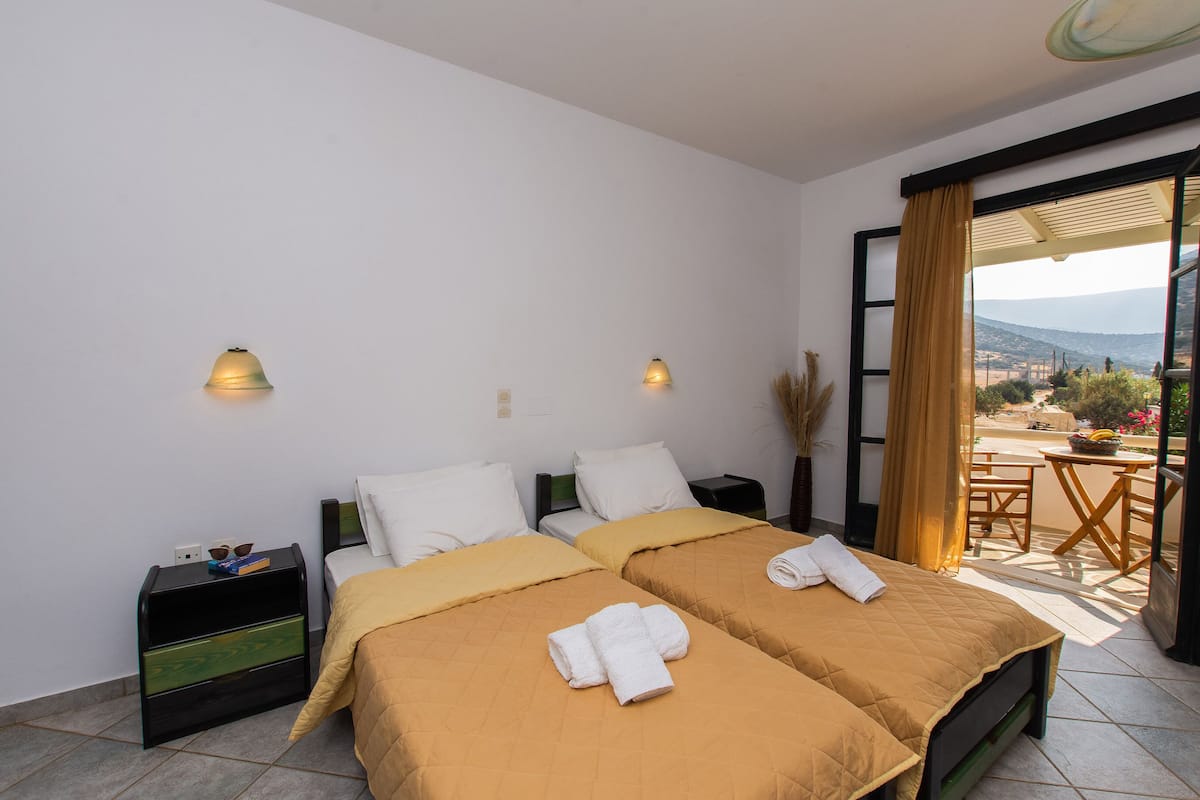 Habitación de hotel con dos camas, una mesita y un balcón con vistas.