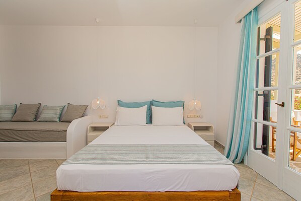 A bedroom with a bed, a sofa, a nightstand, and a door leading to an outdoor area. - Studio Strouvalis (Naxos)