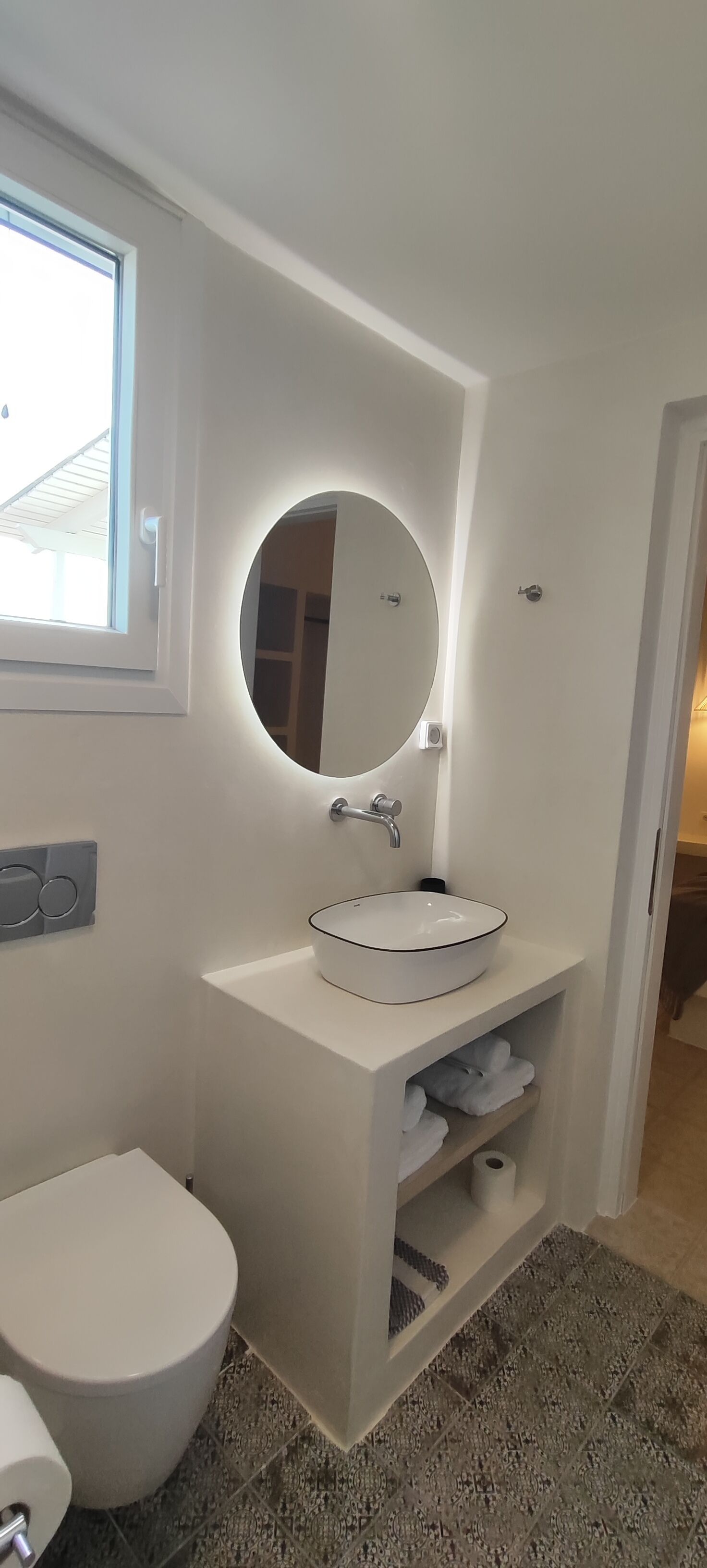 Une salle de bain moderne avec un miroir rond, un lavabo blanc et des toilettes.