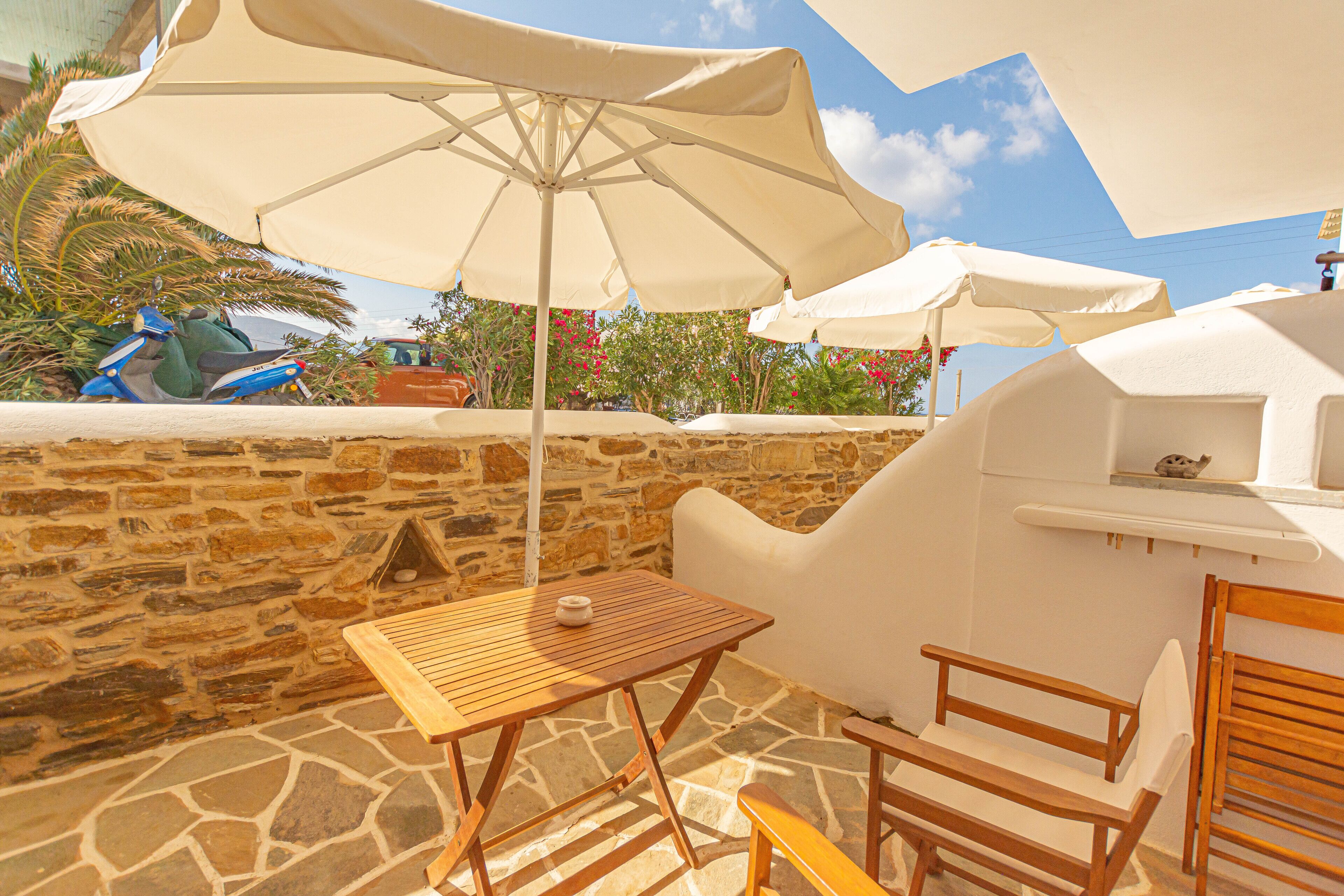 A patio with a stone wall, a wooden table, a wooden chair, and a white umbrella.