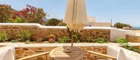 A stone-walled outdoor seating area with a round table and chairs, an umbrella, and potted plants.