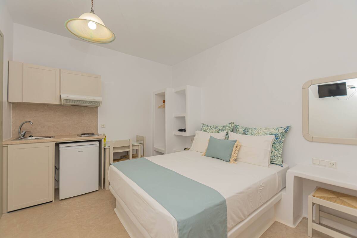 Habitación de hotel pequeña y funcional con cama, escritorio, silla, refrigerador pequeño y televisión integrada.