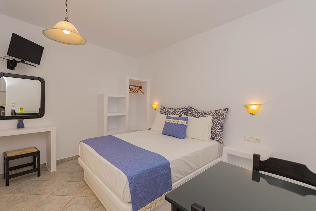 Un dormitorio con cama, mesitas de noche, televisor e iluminación en la pared.