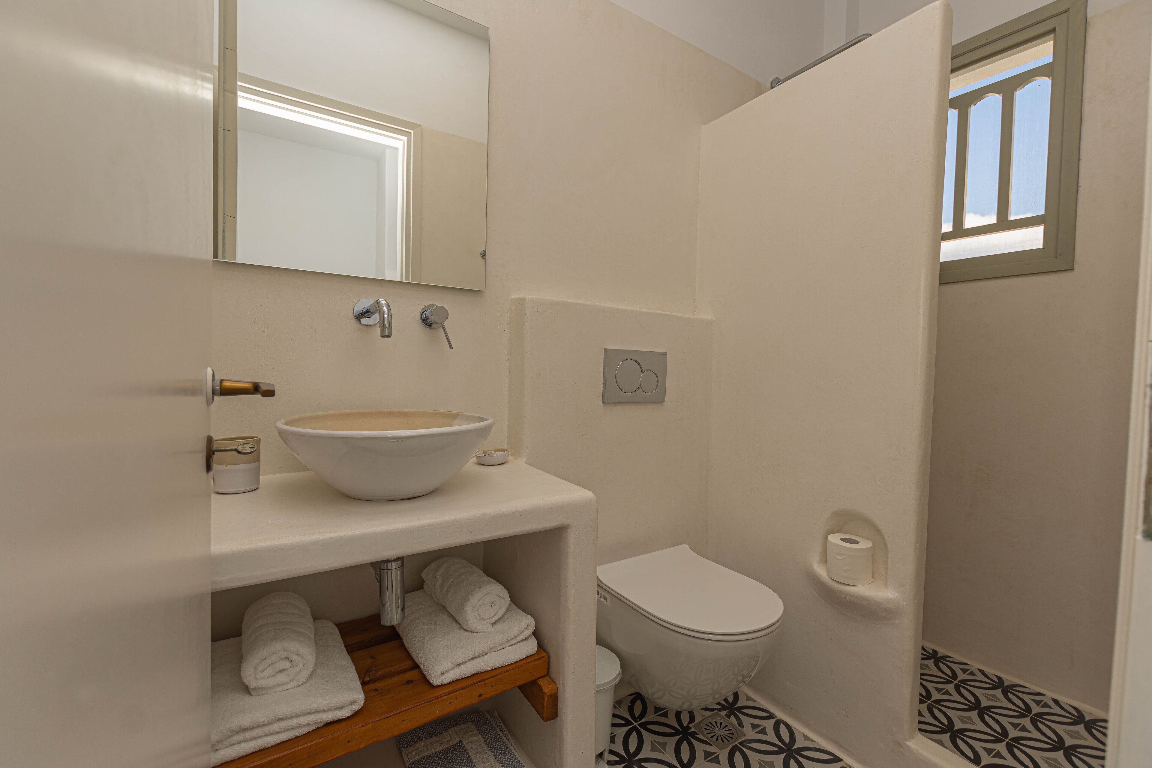 A bathroom with a white sink, mirror, and toilet. There are towels on a shelf and a shower door with a window.