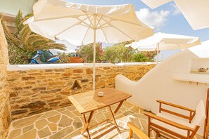 A stone-walled patio with a wooden table and two wooden chairs, an umbrella, and a barbecue grill. - Studio Strouvalis (Naxos)