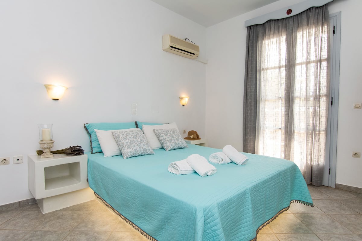 Un dormitorio con cama, lámparas de noche, mesita de noche, aire acondicionado y una ventana con cortinas.
