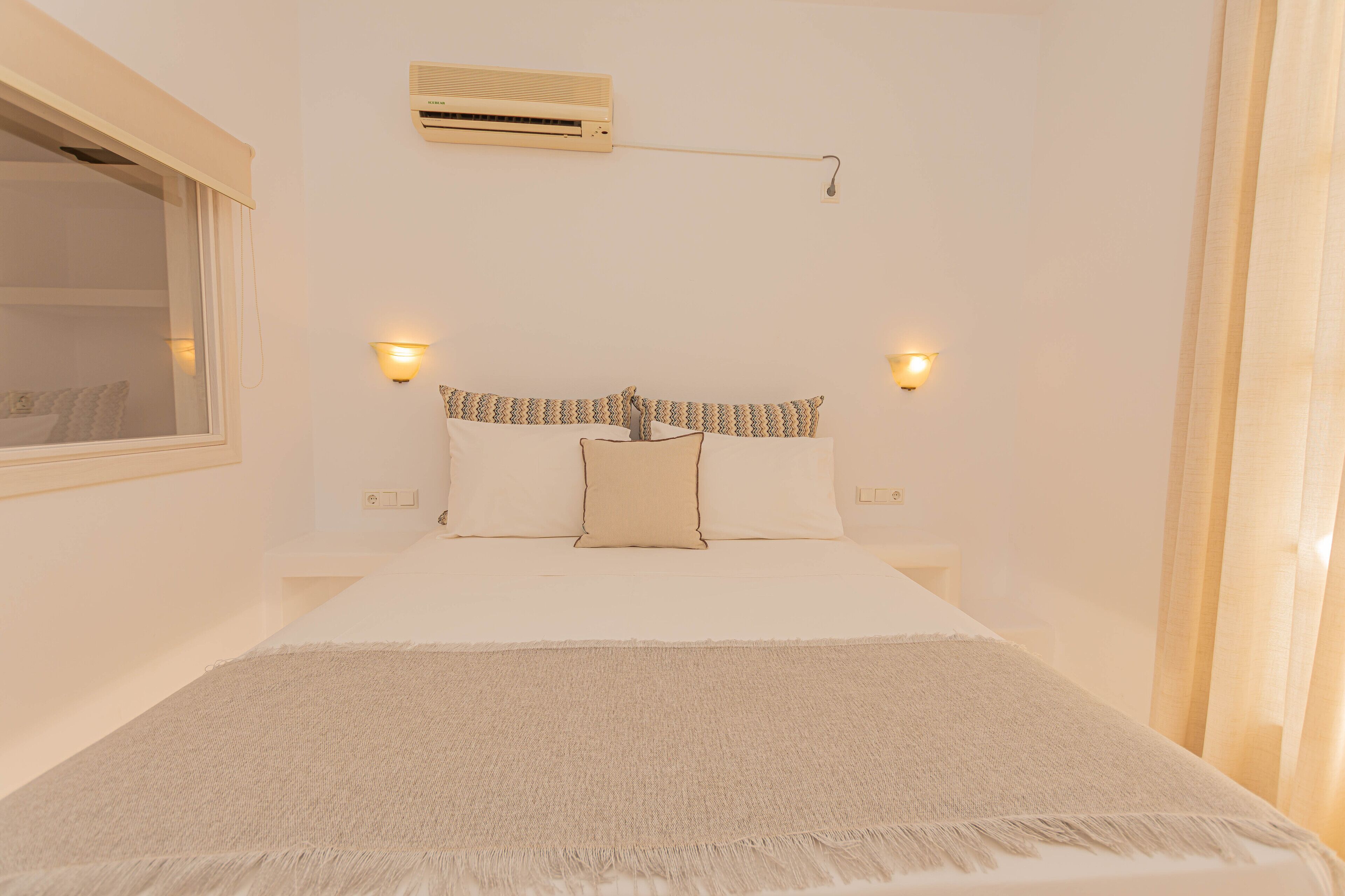 Een slaapkamer met een bed, twee bedlampen, een raam met zonwering en een airconditioning.
