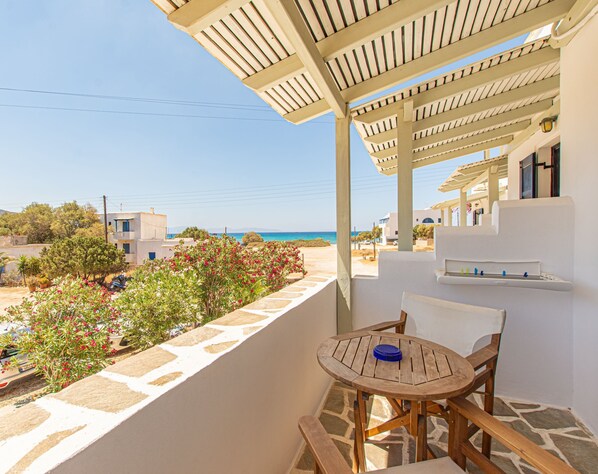 A balcony with a view of the sea, a wooden table and chairs, and a pergola structure. - Studio Strouvalis (Naxos)
