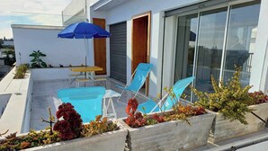 Ein moderner Außenbereich mit blauen Stühlen und einem Tisch, einem blauen Sonnenschirm und Kübelpflanzen.