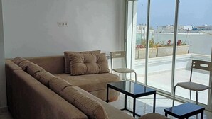 Ein modernes Wohnzimmer mit einer großen Couch, zwei kleinen Tischen und Blick auf die Stadt durch große Fenster.