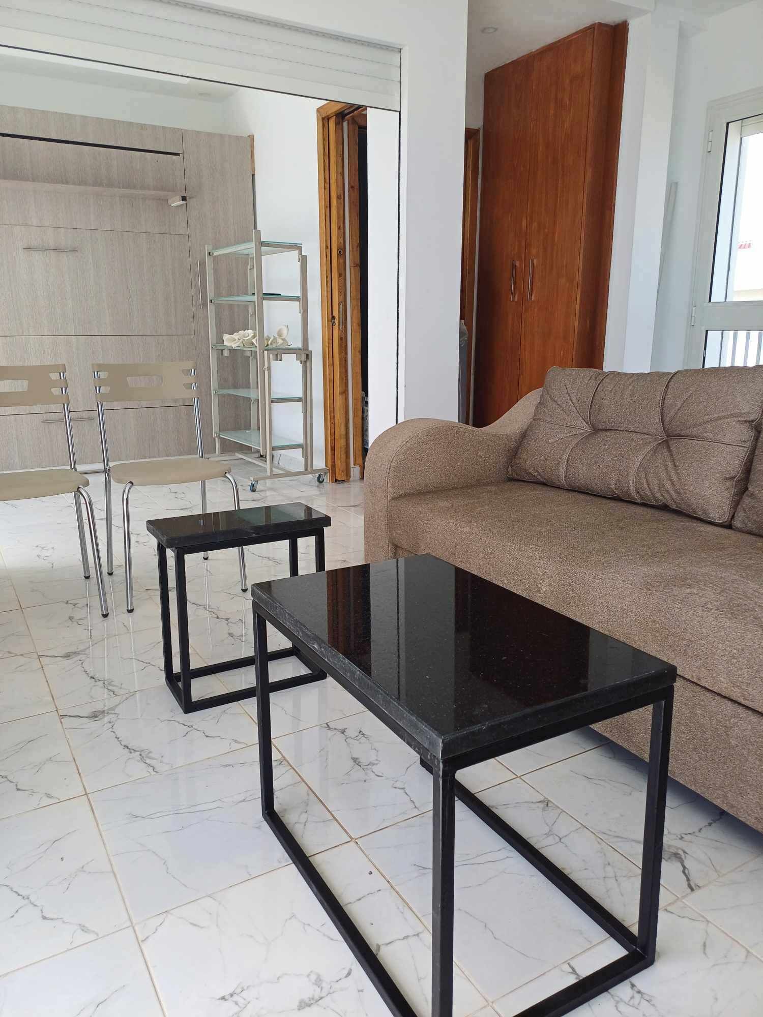 A modern living room with a sofa, two black tables, and a glass shelving unit.