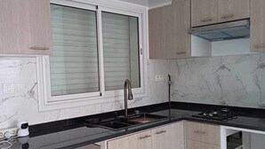Eine moderne Küche mit hellen Holzschränken, einer schwarzen Arbeitsplatte, einem eingebauten Herd und einem Fenster mit Jalousien.