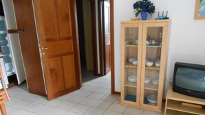 A room with a wooden cabinet containing bowls, a television on a stand, and a door leading to another room. - Holidays apartment in Limone sul Garda- first floor, right side (Limone Sul Garda)