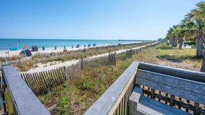 A beach with a wooden fence, a pier in the background, and a clear blue sky. - Spacious, Bay View - Close to Boardwalk, Location! (Myrtle Beach)