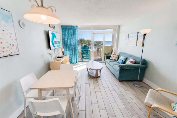 Un salon moderne avec un coin repas, un canapé de couleur turquoise et une vue sur la mer grâce à de grandes portes vitrées.