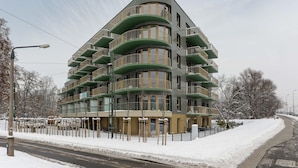 Un edificio residencial de varios pisos con balcones, suelo cubierto de nieve y cielo despejado.