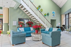 A spacious lobby with a staircase, two sofas, and potted plants.