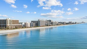 A coastal cityscape with a beachfront hotel, a sandy beach, and a clear blue sky. - New, Caravelle Resort, Amazing Oceanview, Updated! (Myrtle Beach)
