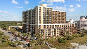 A multi-story hotel with a central courtyard, surrounded by palm trees and a beach. - New, Caravelle Resort, Amazing Oceanview, Updated! (Myrtle Beach)
