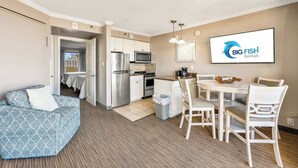 A modern kitchen with stainless steel appliances, a dining area with white furniture, and a large screen displaying 'Big Fish Rentals' logo. - New, Caravelle Resort, Amazing Oceanview, Updated! (Myrtle Beach)