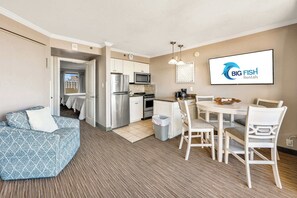 A modern kitchen with stainless steel appliances, a dining area with white furniture, and a large screen displaying 'Big Fish Rentals' logo.