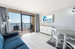 Una sala de estar moderna con balcón, comedor y un televisor que muestra 'BIG FISH RENTALS'.