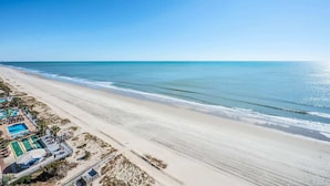 Een strand met heldere lucht, een zandstrand en een zwembadgedeelte met ligstoelen.