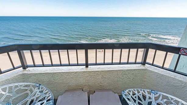 Een balkon met twee metalen stoelen, uitzicht op het strand en een rookvrij bord.