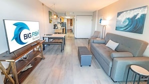 Een moderne woonkamer met een flatscreen televisie, een grijze bank, een salontafel en een schilderij van een golf op de muur.