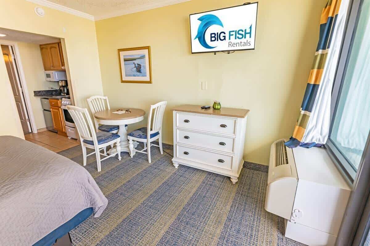 Une chambre d’hôtel comprenant un lit, un bureau avec deux chaises, une commode, un téléviseur et une kitchenette.