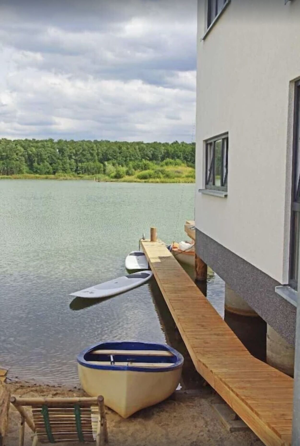 Blick auf ein Seeufer mit einer hölzernen Anlegestelle, einem Boot und einem Gebäude mit einem Fenster.