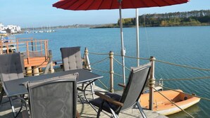 Une terrasse avec des sièges extérieurs, un parasol rouge et une vue sur l’eau.