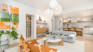 Ett modernt vardagsrum med en grå soffa, trästolar, ett soffbord och en köksdel med barstolar.