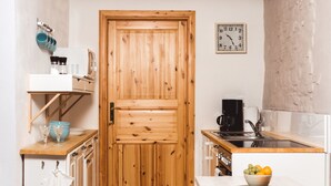 Een kleine keuken met een houten deur, een koffiezetapparaat, een spoelbak en een fruitschaal op het aanrecht.
