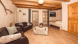 Een gezellige woonkamer met een bruine leren bank, een kleine witte tafel en een houten bed.